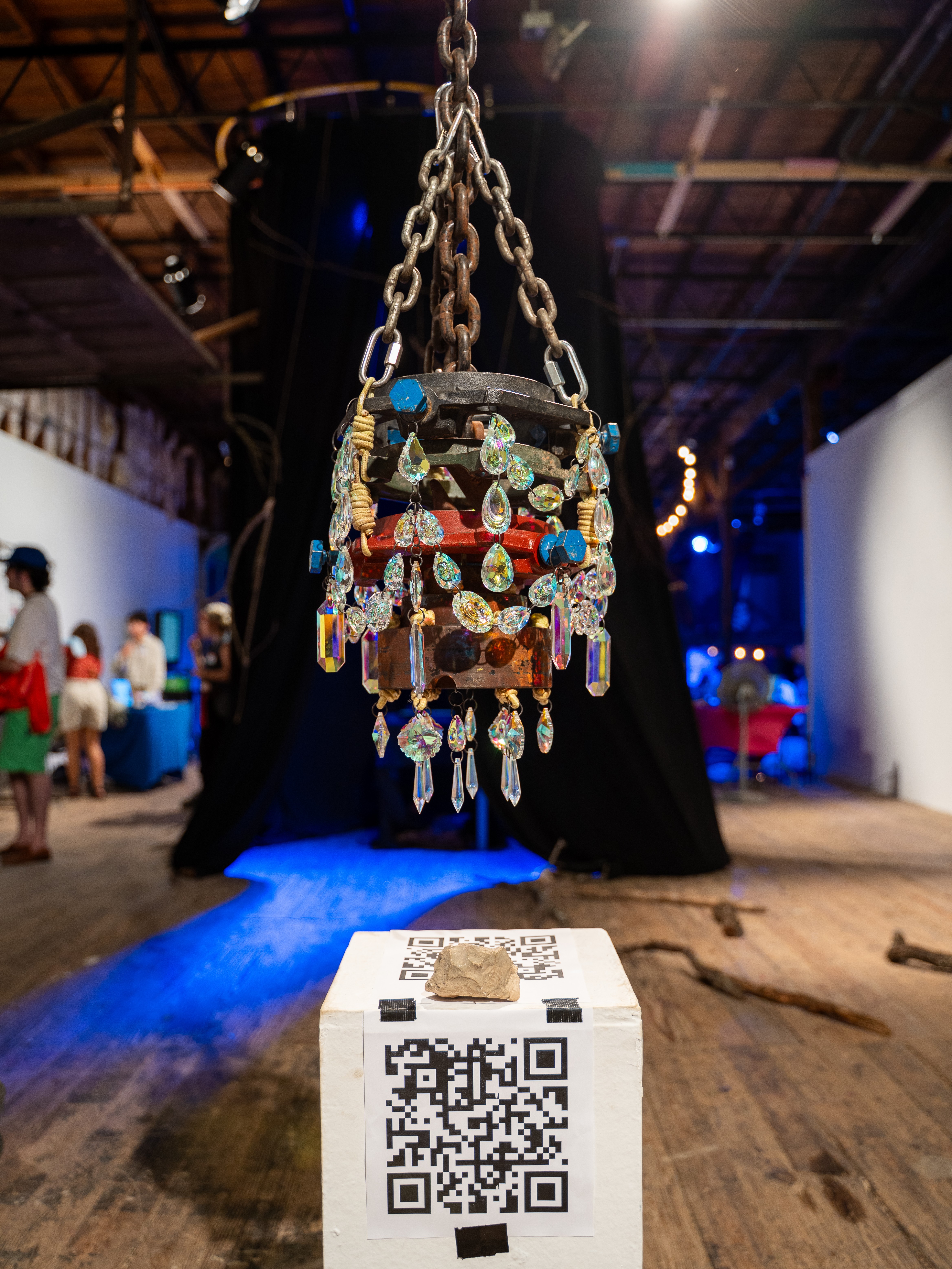 Sculpture suspened from ceiling above a pedastal with a QR code