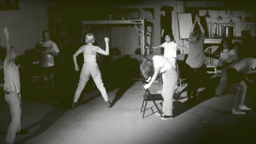 Still from dance video. Figures in various static, geometric poses