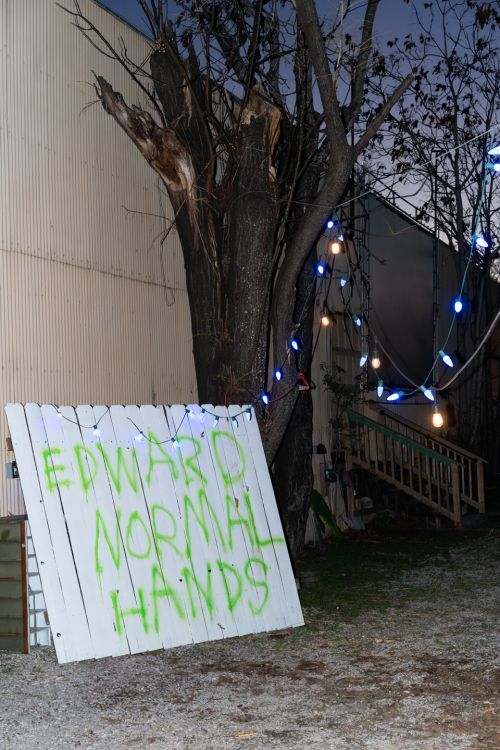 Edward Normalhands spray painting in green on a sign outside MoHA